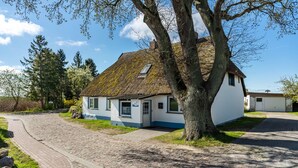 Ett traditionellt hus med ett halmtak, en asfalterad uppfart och ett stort träd framför.