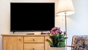 En platt-TV monterad på ett träskåp, en lampa och en stol med en krukväxt i förgrunden.