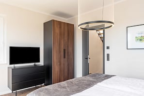 Ein modernes Schlafzimmer mit einem Bett, einem Fernseher auf einer Kommode, einem Holzschrank und einer Hängeleuchte.
