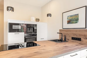 A modern kitchen with a wooden countertop, built-in appliances, and a framed painting on the wall.