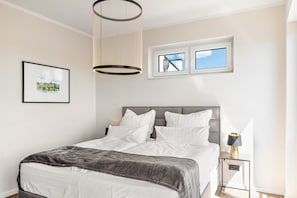 A bedroom with a bed, a bedside table with a lamp, a window, and a picture on the wall.