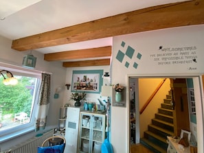 Quarto aconchegante com teto de madeira, janela com cortinas, estante de livros, escada e uma frase decorativa na parede.