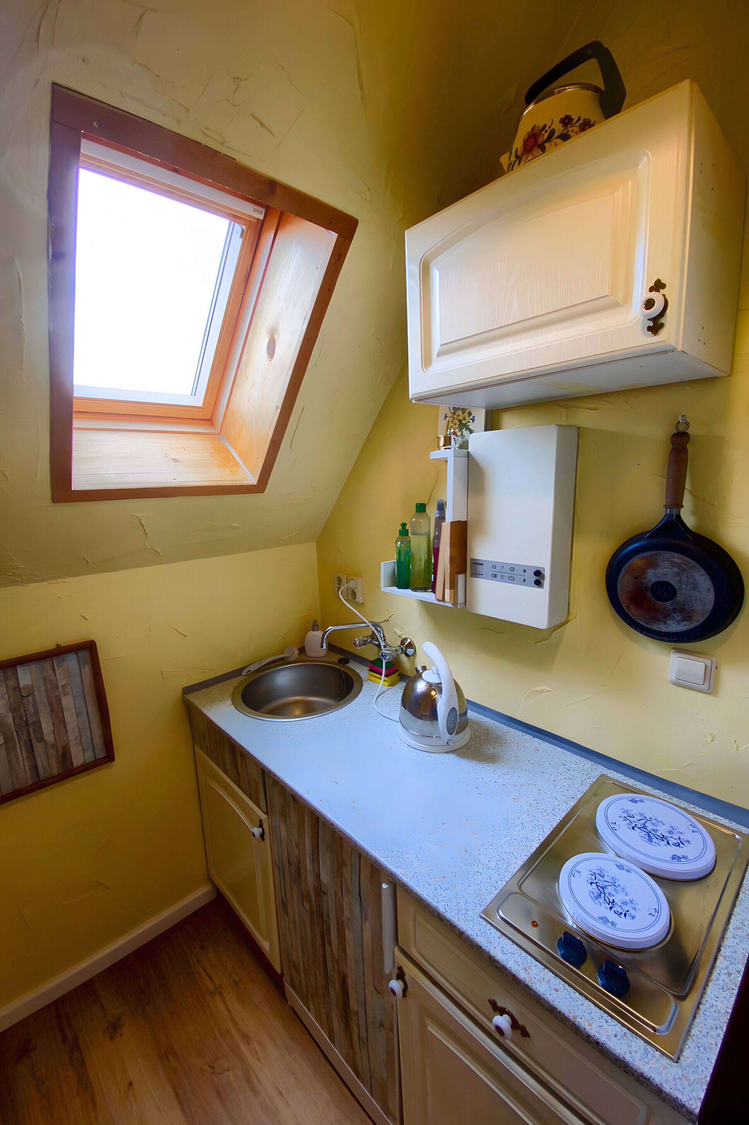 A kitchen with a skylight, a stove, a sink, and a hanging pan.