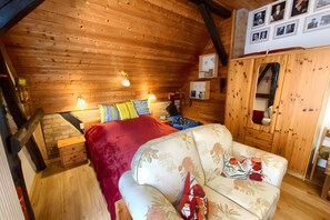 Una habitación acogedora con techo de madera, una cama con manta roja, un sofá floral y un armario de madera.