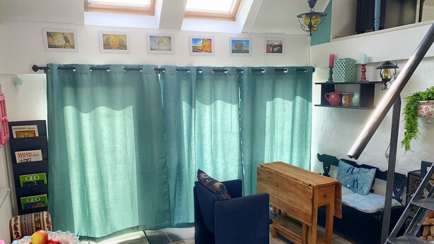 Een gezellige kamer met een houten tafel, een blauwe bank, een trap en een groen gordijn.