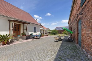 Ein Innenhof mit Kopfsteinpflaster, ein weißes Gebäude mit rotem Dach und ein Ziegelgebäude mit Solaranlage.