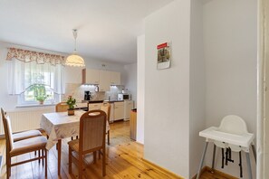 Eine Küche mit Holzboden, einem Esstisch mit Stühlen, einem weißen hochstuhl für Babys und einem Fenster mit Vorhängen.