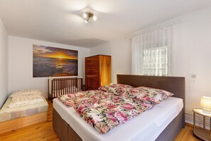 Ein Schlafzimmer mit einem Bett, einem Babybett, einem Gemälde, einem Fenster mit Vorhängen und einer Nachttischlampe.