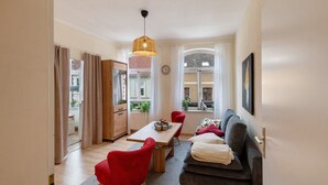 A modern living room with a sofa, red chairs, a dining table, and a hanging light fixture.