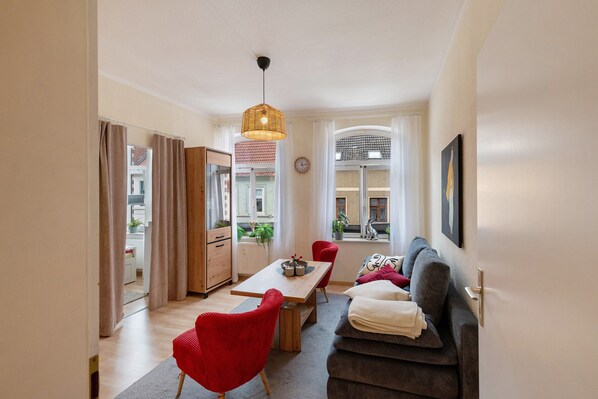 A modern living room with a sofa, red chairs, a dining table, and a hanging light fixture.