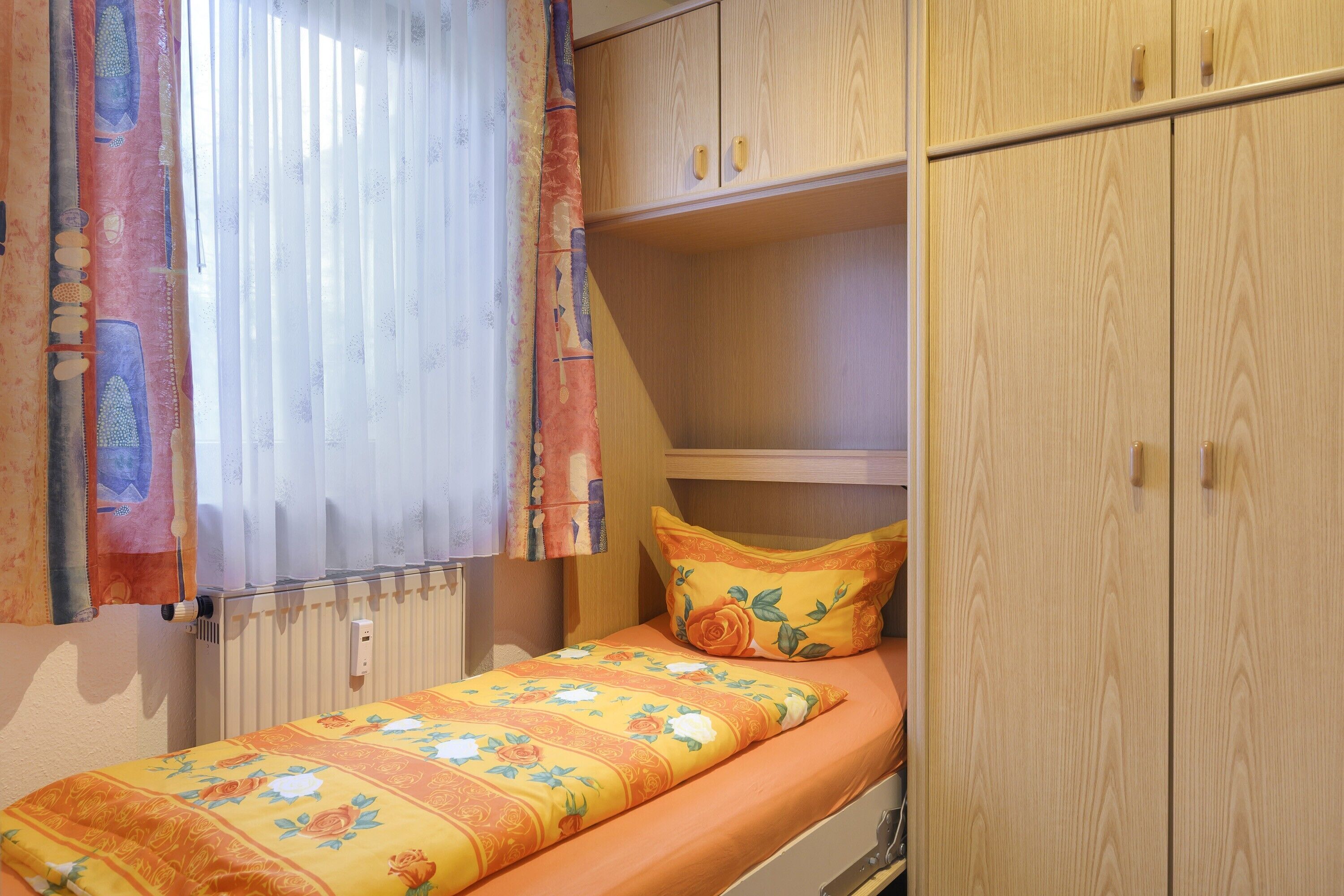 Una cama individual con una colcha estampada, un armario de madera y un radiador.
