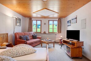 A cozy room with a bed, a sofa, a TV on a wooden stand, and a window with curtains.