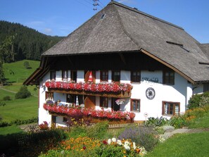 A traditional Alpine-style building with a balcony adorned with flowers, a clock, and a sign indicating the establishment's name and year.