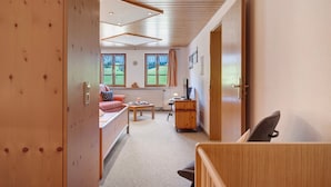 Ein Zimmer mit Holzbalkendecke, einem Bett, einem Schreibtisch, einem Stuhl und einem Fenster mit Blick auf Grünfläche.