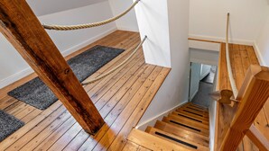 Una escalera de madera con barandilla de cuerda, pasamanos de madera y rellano alfombrado.