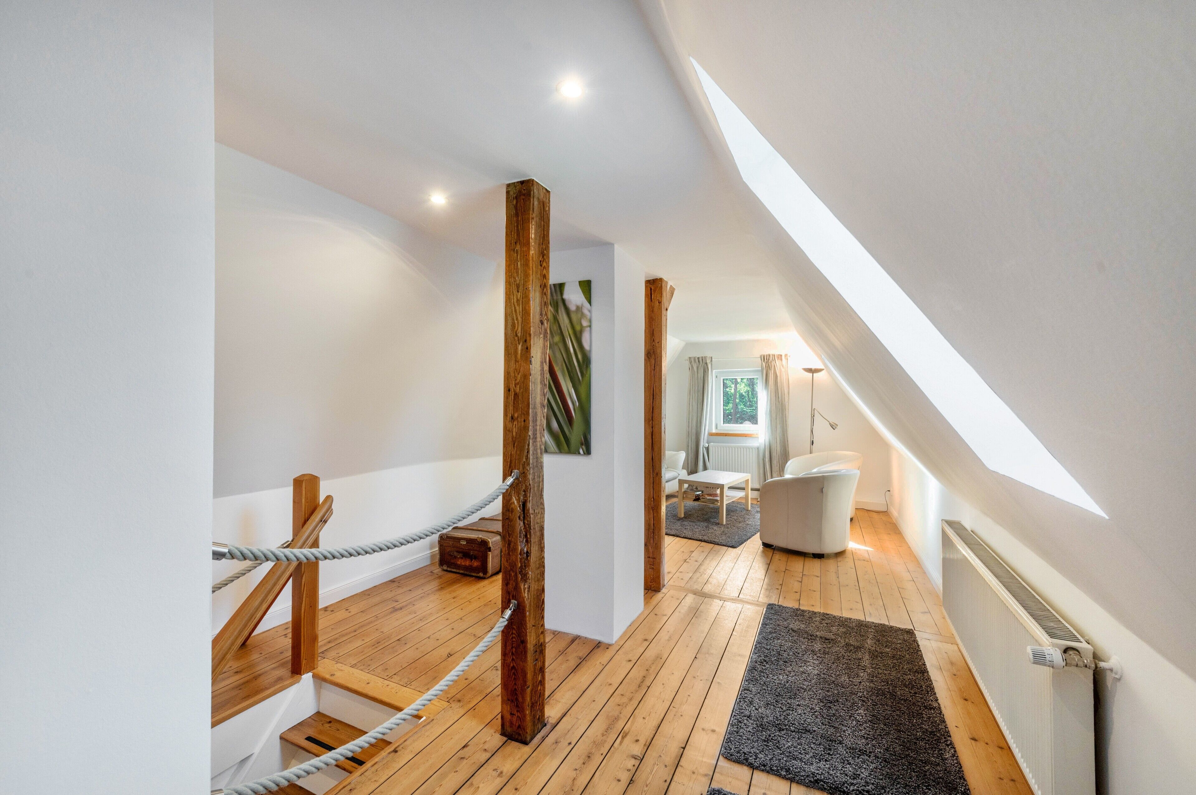 Un intérieur moderne avec un escalier en bois, un mur blanc, un tapis noir, une chaise blanche et une fenêtre avec des rideaux.
