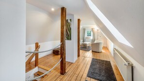 Un interior moderno con una escalera de madera, una pared blanca, una alfombra negra, una silla blanca y un ventanal con cortinas.