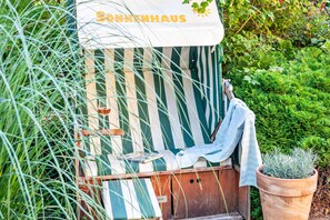 Un espace extérieur accueillant avec des sièges confortables, un auvent à rayures et un pot de fleurs.