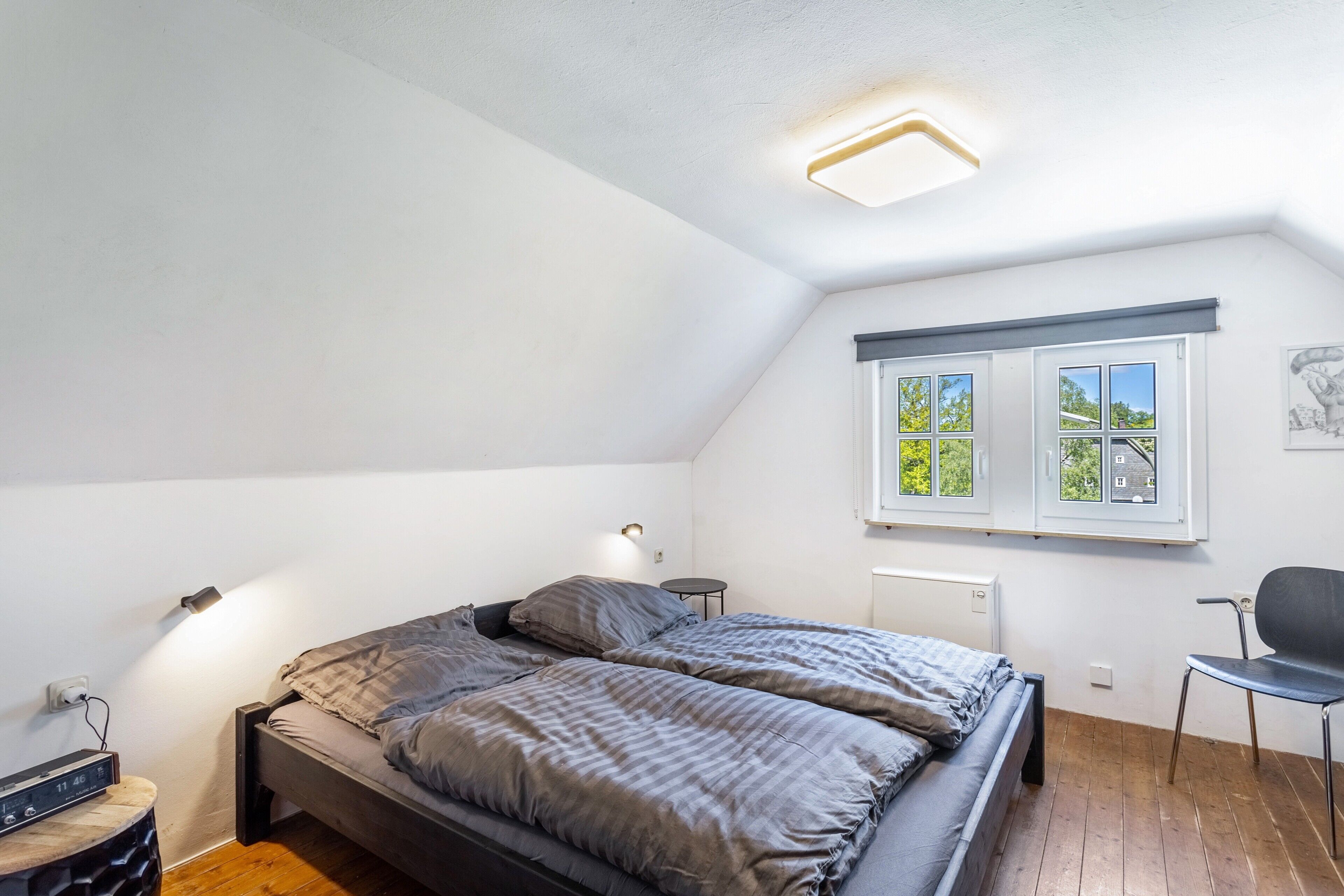 A bedroom with a bed, bedside tables, a chair, and a window with a view of trees.