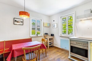 A kitchen with a stove, a table with a red tablecloth, wooden chairs, a hanging light fixture, and a window with a view of greenery. - Apartment 'Anno 1960' with Mountain View, Private Terrace and Wi-Fi (Bestwig)