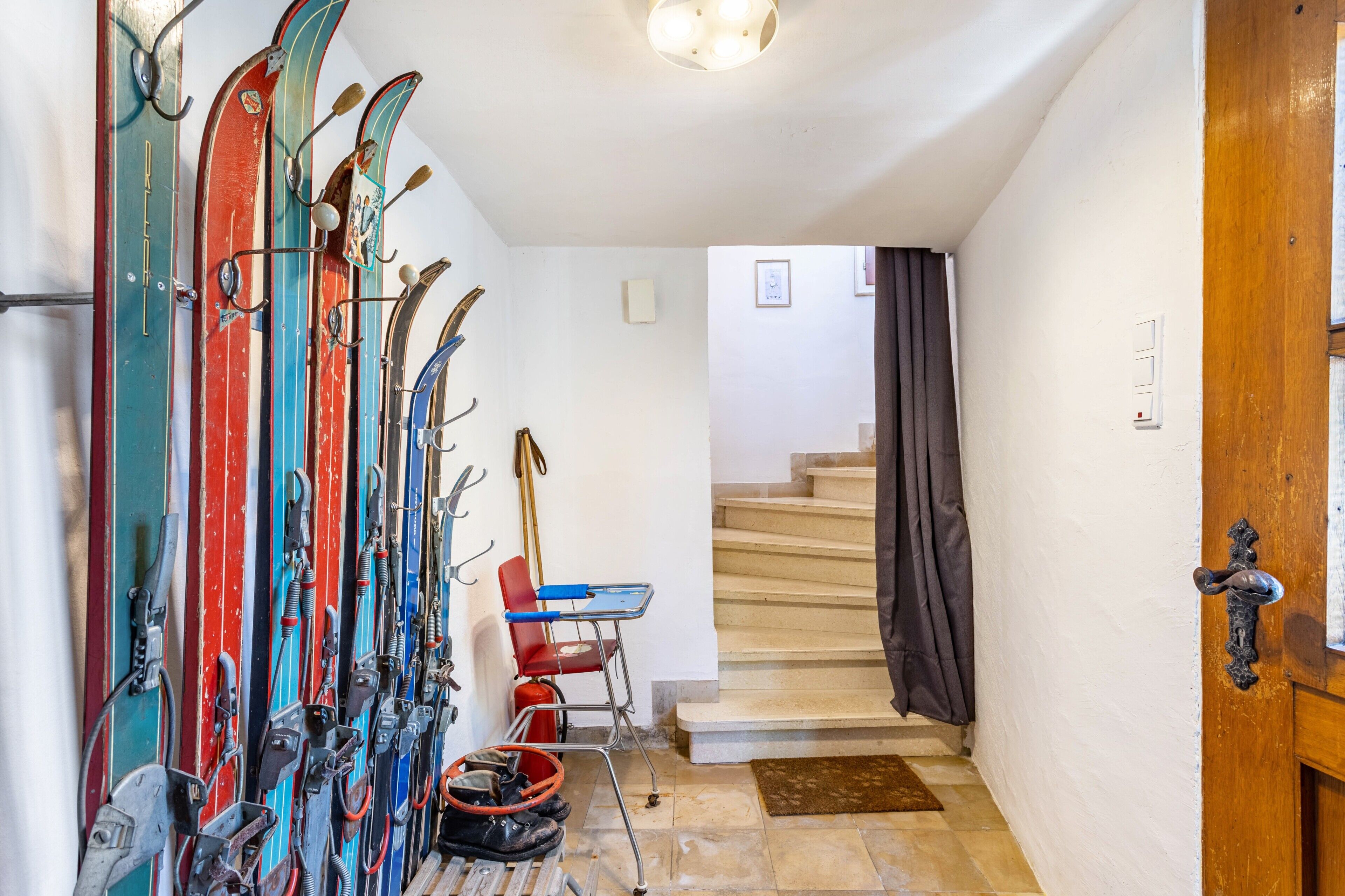 Een gang met ski's, skiërs stokken, een stoel, een brandblusser en een trap.