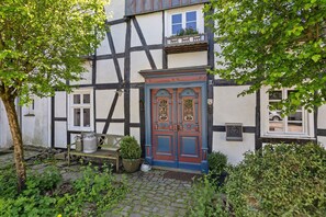 Un bâtiment traditionnel à colombages, avec une porte bleue, un banc et des plantes en pot.