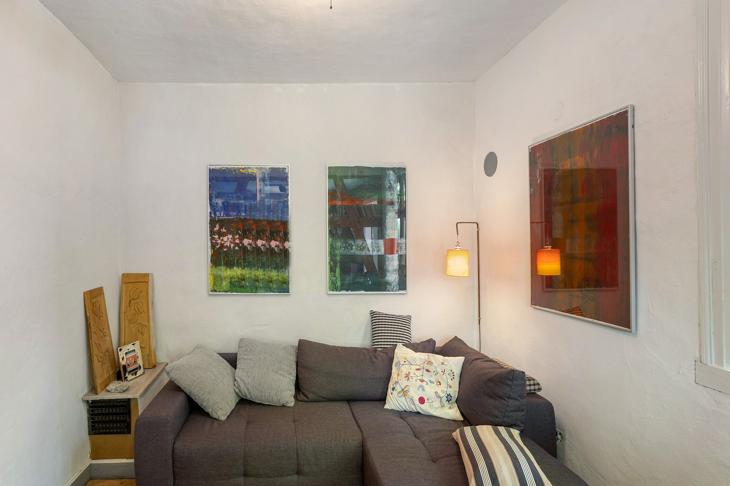 A living room with a sofa, cushions, a lamp, and abstract art on the walls.