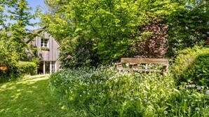 Ein Holzhaus, umgeben von üppiger Vegetation und einer Holzbank.