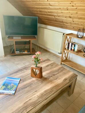 A room with a wooden table, a vase with flowers, a bookshelf, and a television.
