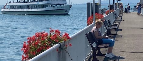 Un muelle con bancos y un barco al fondo.