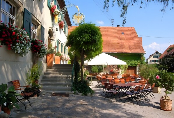 An outdoor café with tables and chairs, a staircase leading to a building, and potted plants.