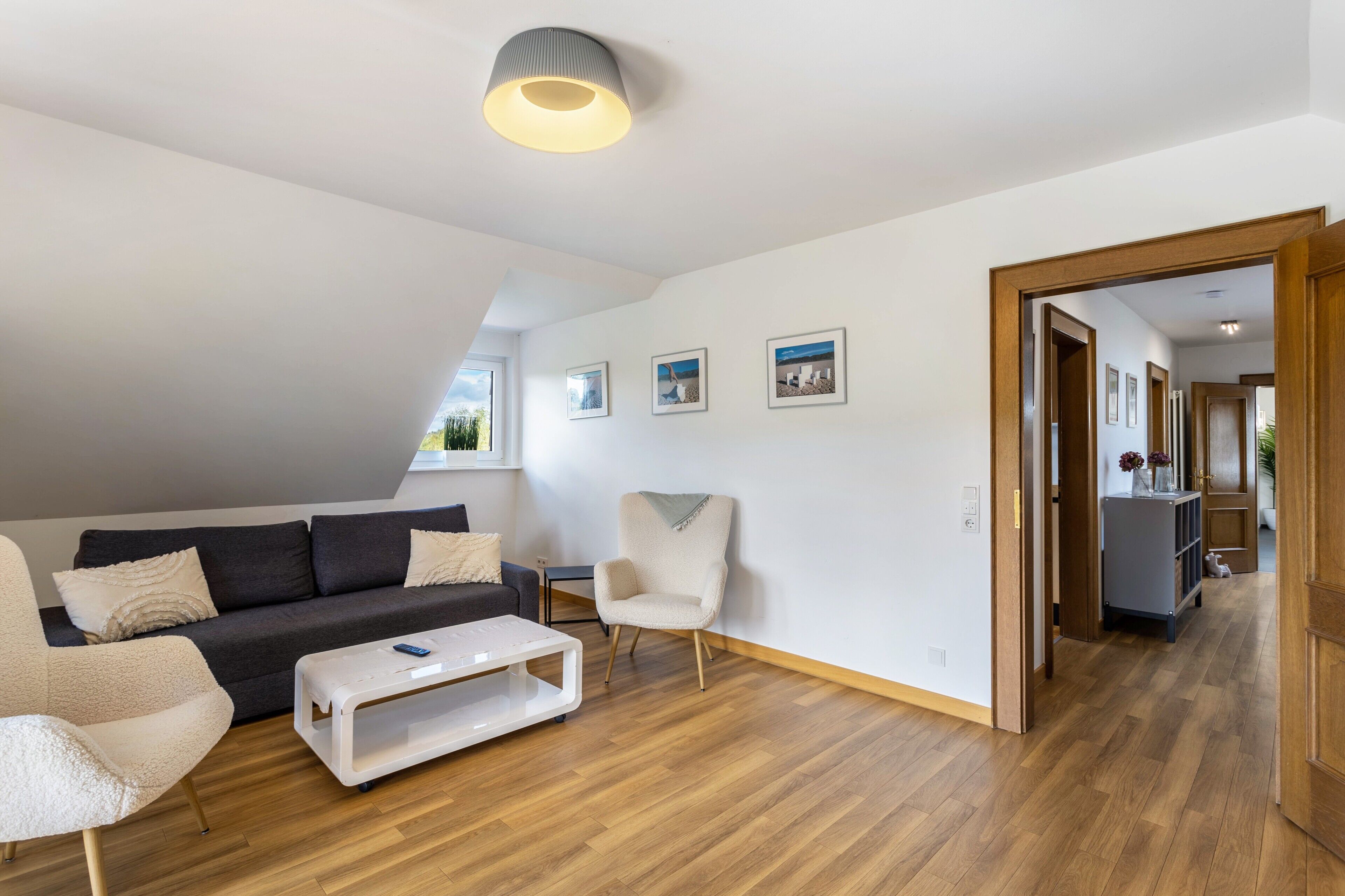 Ein modernes Wohnzimmer mit einem dunklen Sofa, einem weißen Sessel, einem Couchtisch und Holzboden.