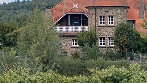 Een gebouw van steen met een rode dakbedekking, een balkon en uitzicht op een beboste heuvel.