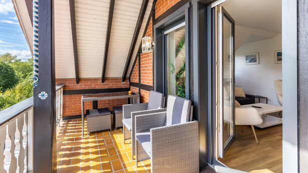 Een balkon met rieten meubilair, een tafel en een schuifdeur naar een binnenruimte.