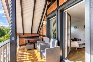 Un balcon doté de meubles en osier, d’une table et d’une porte-fenêtre coulissante donnant sur un espace de vie intérieur.