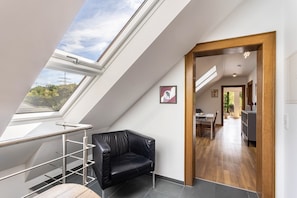 Un intérieur moderne avec une verrière, un fauteuil en cuir noir, un coin repas et une cuisine.