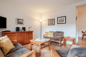 A living room with a sofa, two armchairs, a coffee table, a wooden cabinet, and a flat-screen TV.