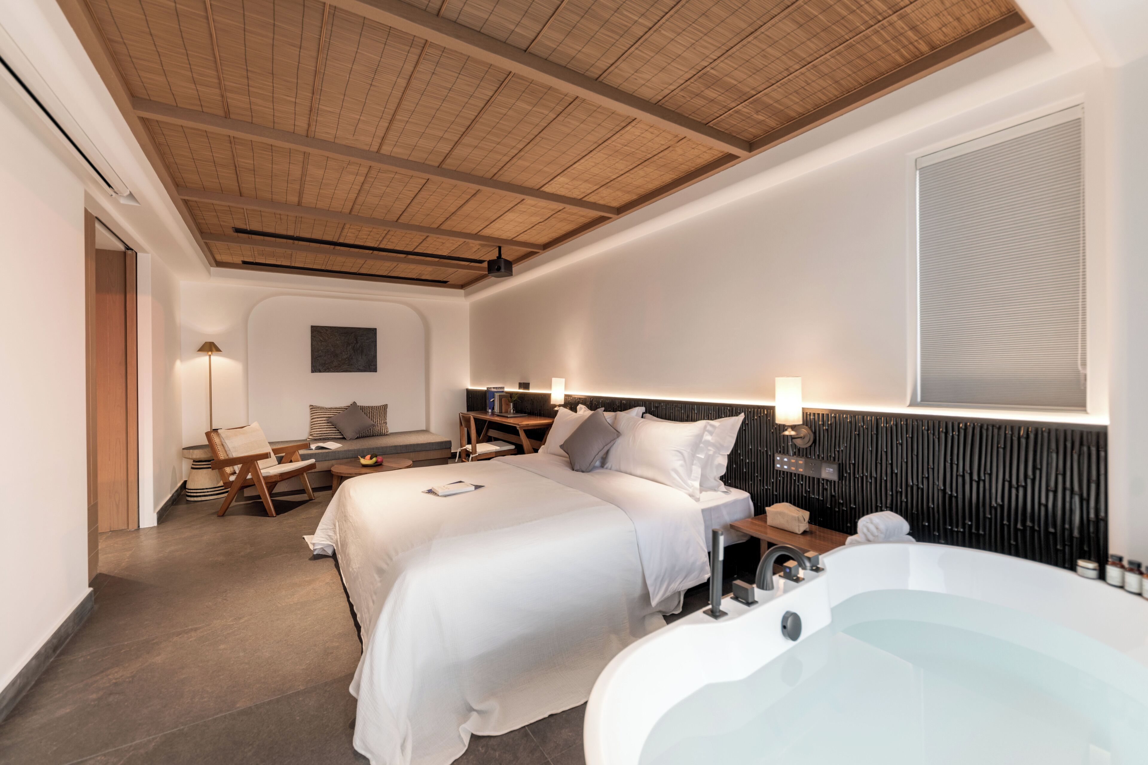 Une chambre d’hôtel moderne dotée d’un grand lit, d’un coin salon séparé, d’un bureau et d’une salle de bain séparée avec baignoire.