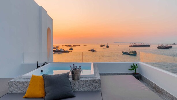 Balcón con vista al mar al atardecer, que incluye una bañera, cojines y una planta de cactus.
