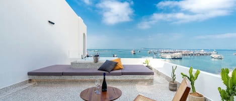 Une terrasse dotée d’un espace salon, d’une table et de chaises, offrant une vue sur une marina où sont amarrés des bateaux.