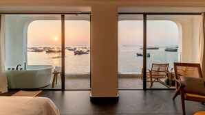 Una habitación con un gran ventanal que ofrece vistas de barcos y el mar al atardecer.