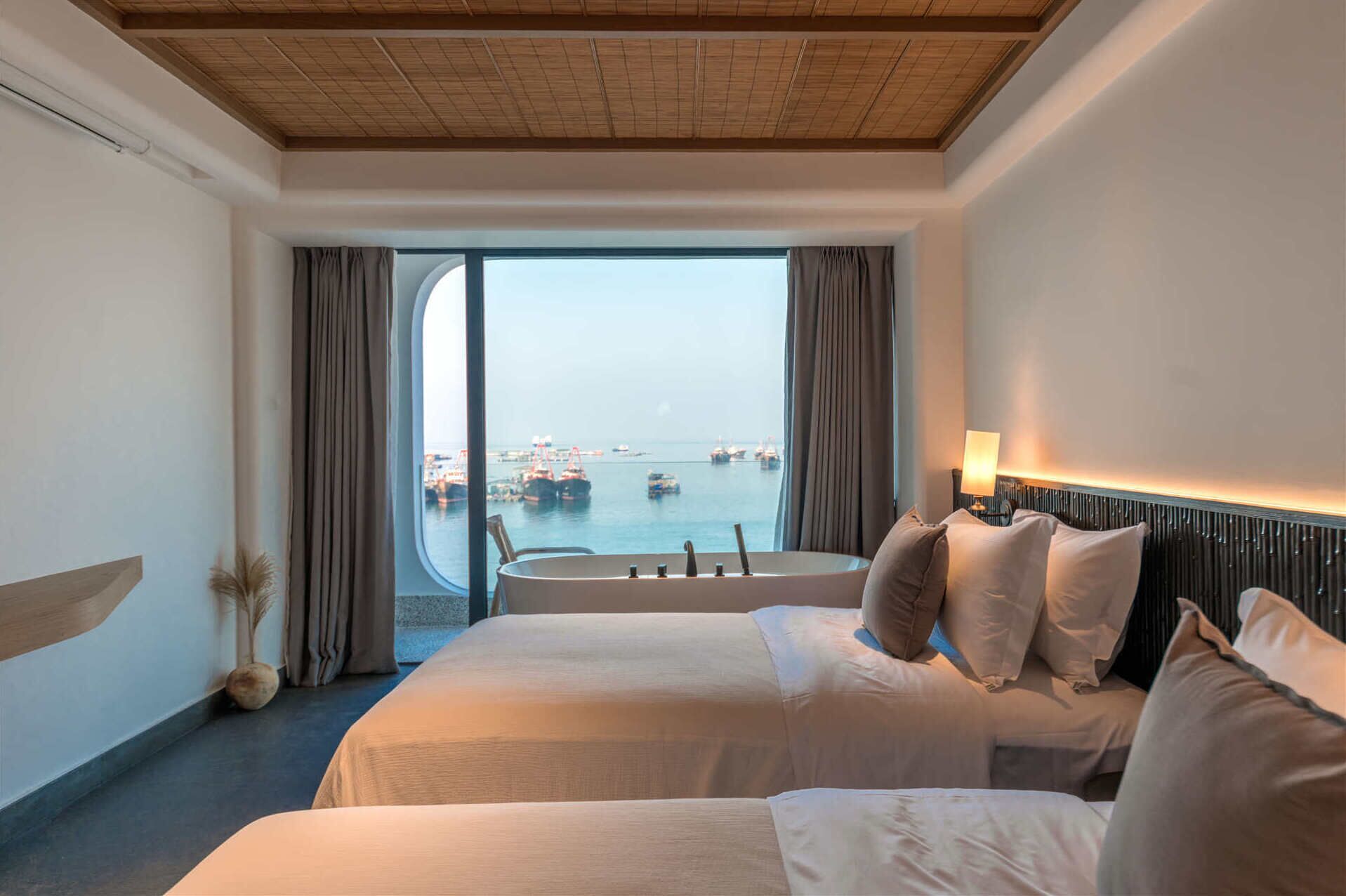 Habitación de hotel con dos camas, vista al mar y un ventanal grande.