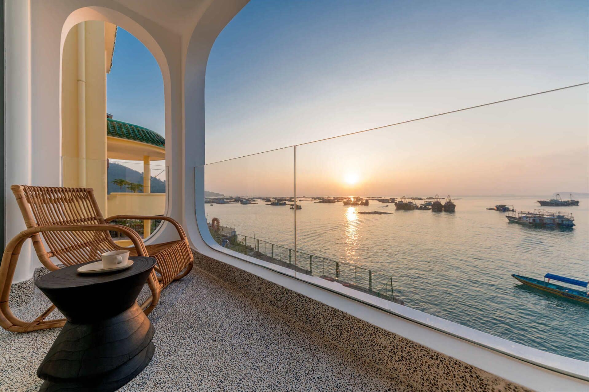 A balcony with a view of the sea at sunset, featuring a chair and a small table.