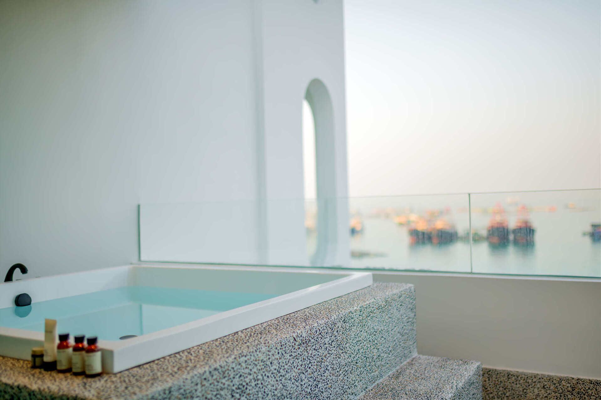 A modern bathroom with a large bathtub, a glass shower enclosure, and a view of the sea.