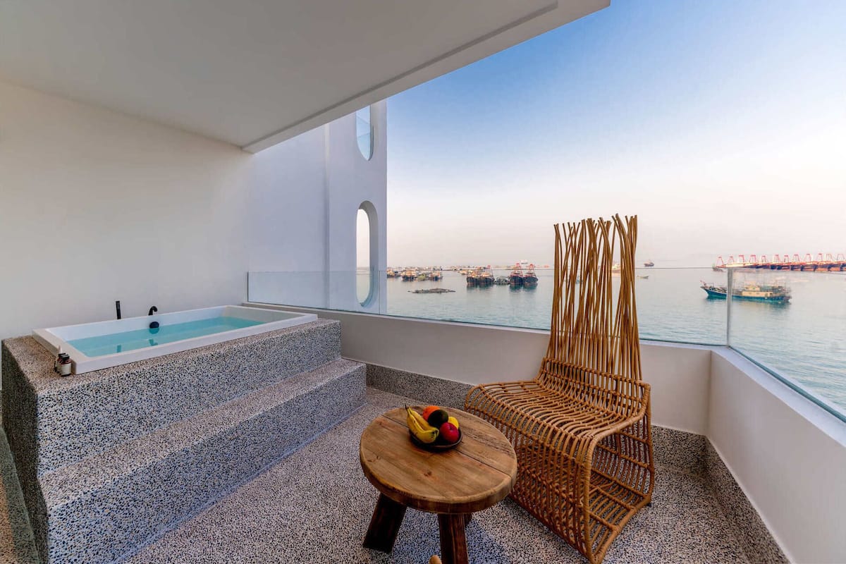 A balcony with a spa tub, a wicker chair, and a table with fruit.