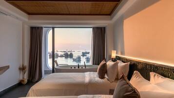 A hotel room with two beds, a large window with a view of boats, a wooden ceiling, and a modern headboard.