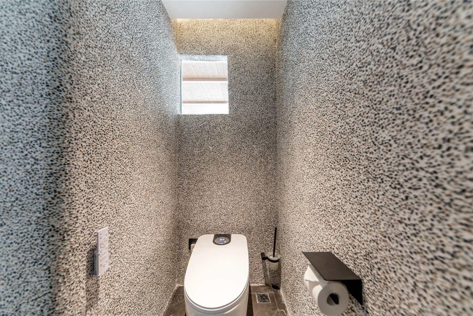 A small, narrow bathroom with a toilet, a sink, and a window providing natural light.