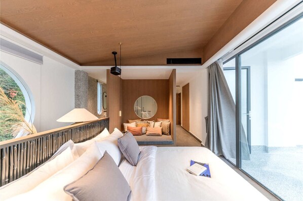 A modern hotel room with a large bed, a round mirror, and a view of the outdoors.