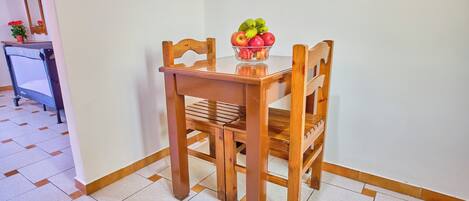 A dining table with chairs, a bowl of fruit, and a potted plant on a tiled floor.