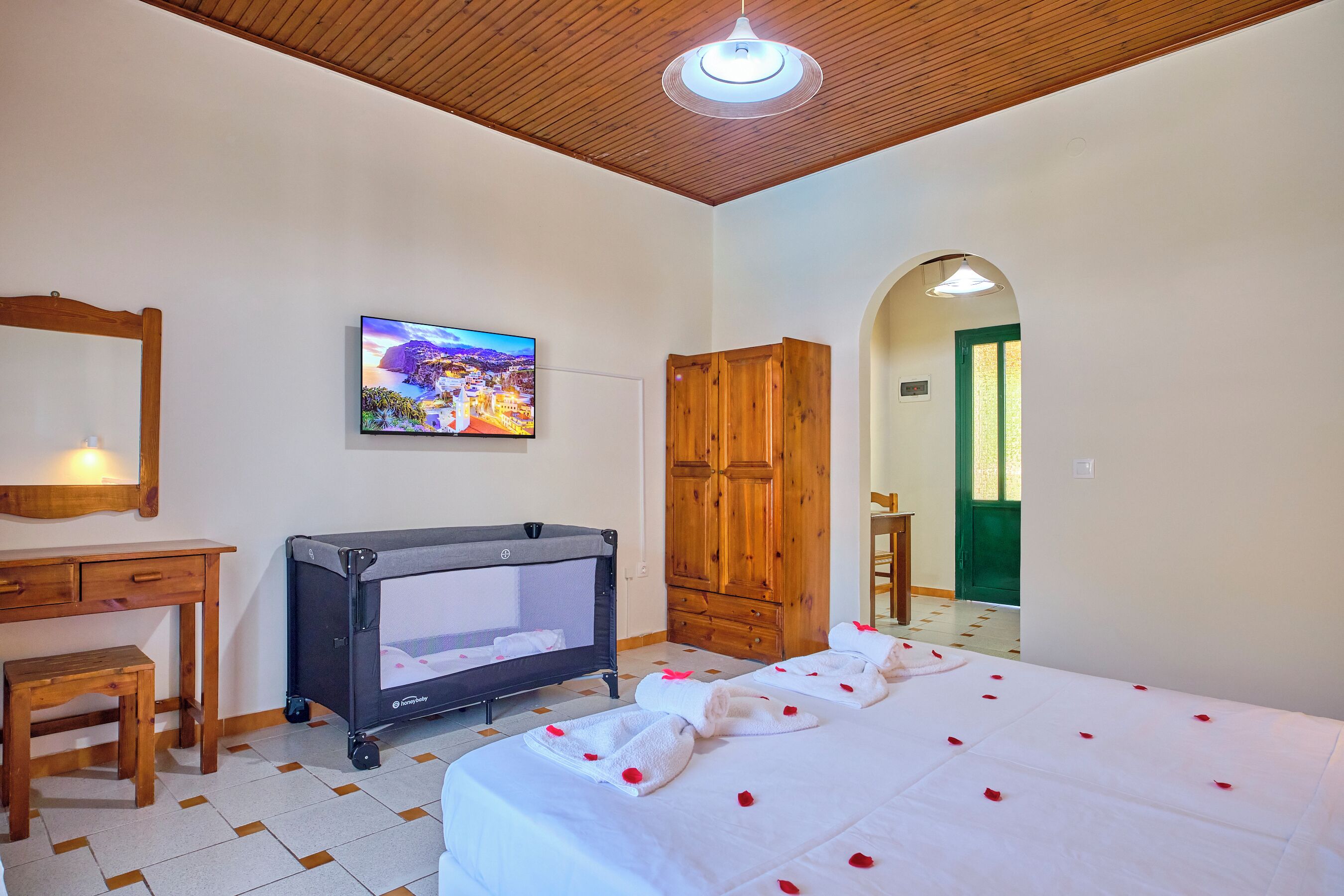 A bedroom with a bed, a crib, a desk, a television, and a wooden wardrobe.
